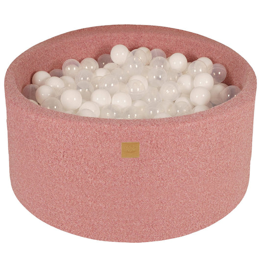 A round, pink boucle fabric ball pit filled with white balls, with a zipper on the side.