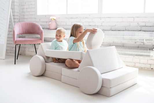 White soft play sofa with two toddlers playing together .