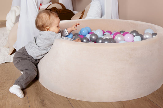 Child playing with colorful balls in a ball pit on a wooden floor.