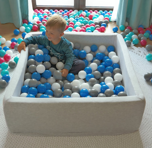 Toddler ball pit with white, grey, and blue balls, toddler smiling at someone off-camera.