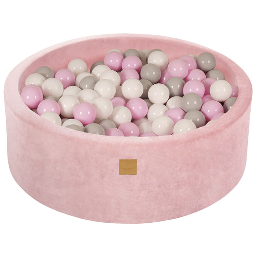 A round pink velvet ball pit filled with multicolored balls, with a zippered cover and a label on the bottom.