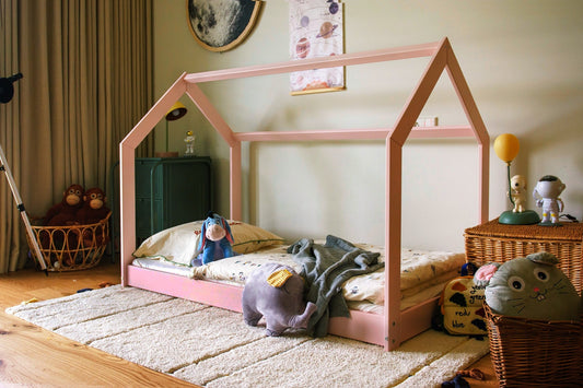 Children's room with a pink house-shaped bed and toys on a wooden floor.