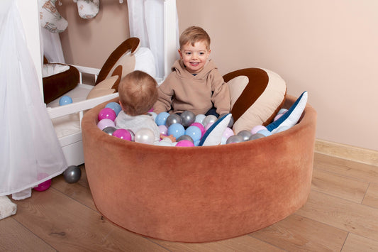 Two children playing with colorful balls in a brown ball pit.