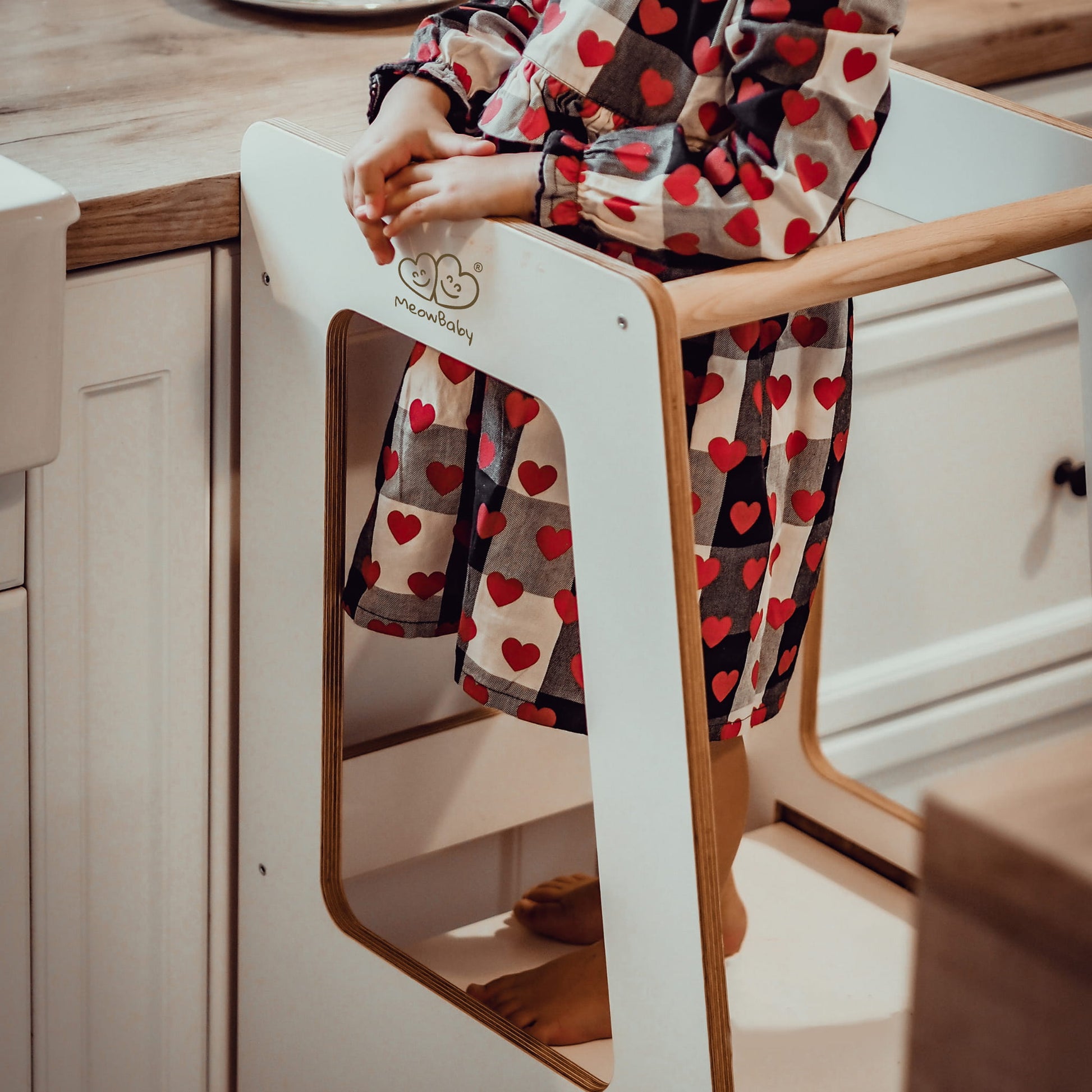Toddler standing on a Meowbaby white wooden kitchen helper in a kitchen setting.