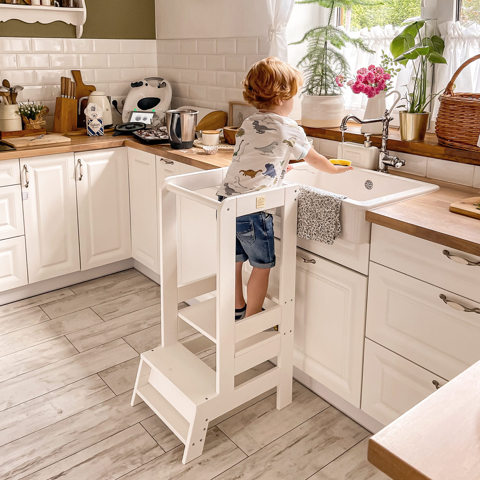 Zoomed-out view of a toddler on a white Meowbaby kitchen helper, washing.