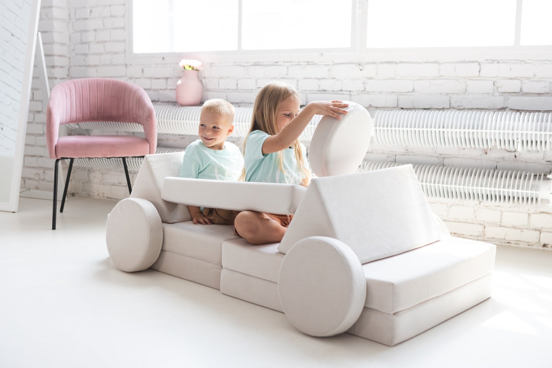 White soft play sofa with two toddlers playing together .