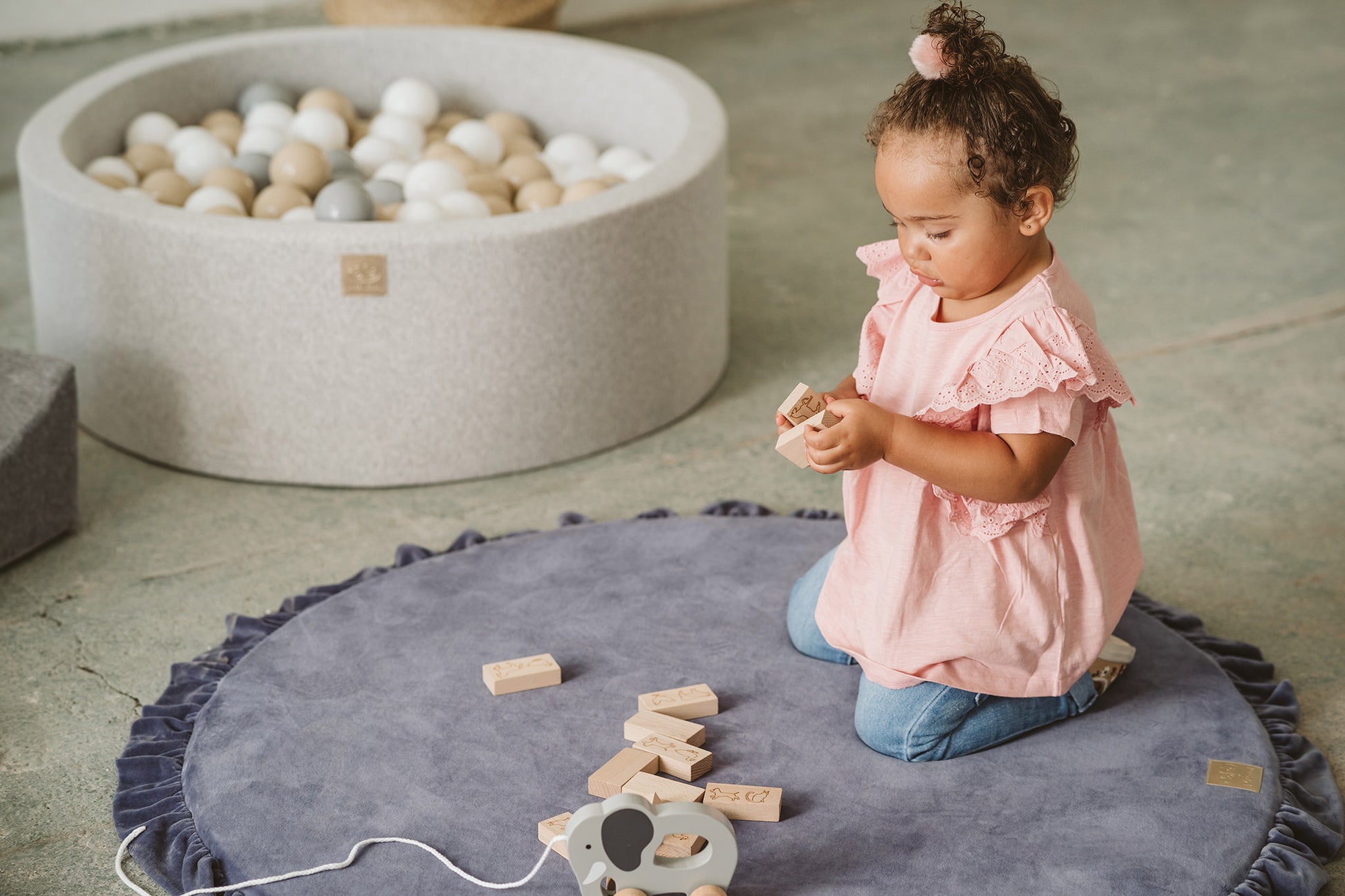 Crushed grey velvet play mat for babies, with one toddler playing and toys in the background.