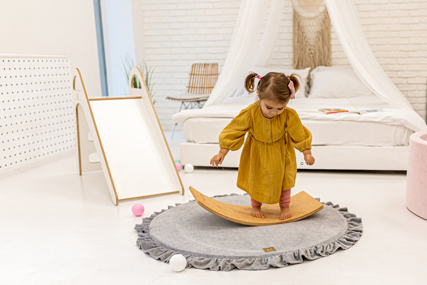 Crushed grey velvet play mat for babies, with a toddler looking down and a ball pit and soft play toys in the background.