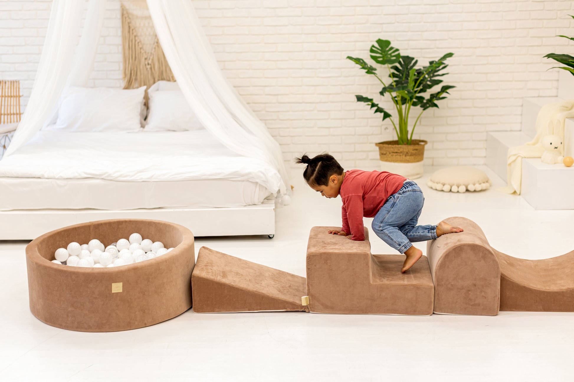 Toddler climbing a brown hoop play set, smiling at someone off-camera while playing.