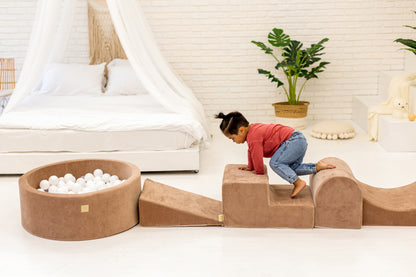 Toddler climbing a brown hoop play set, smiling at someone off-camera while playing.